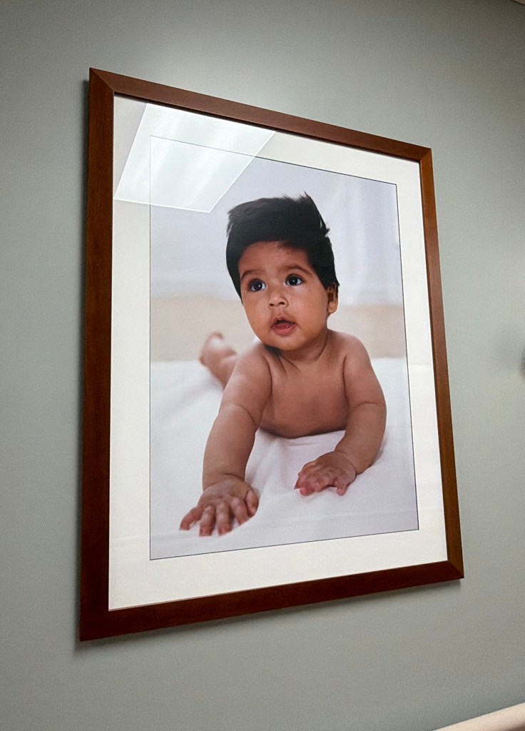 A framed photo of a baby on a bed looking away from the camera with a neutral expression on his face.