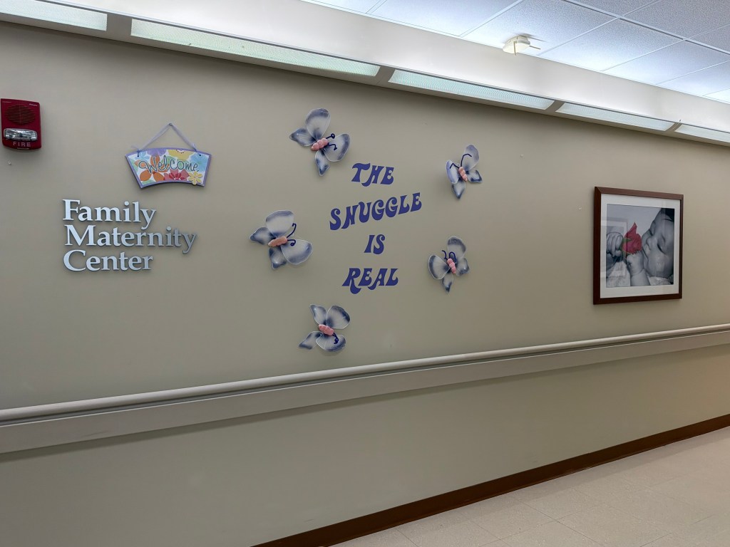 A maternity ward hospital hallway with decorative walls that has a photo of a baby and a welcome sign.